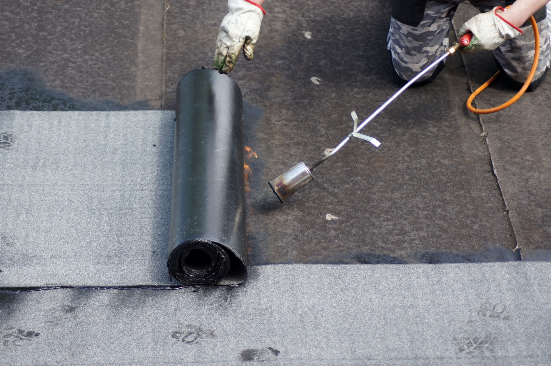 The flat roof installation with propane blowtorch during construction works with roofing felt