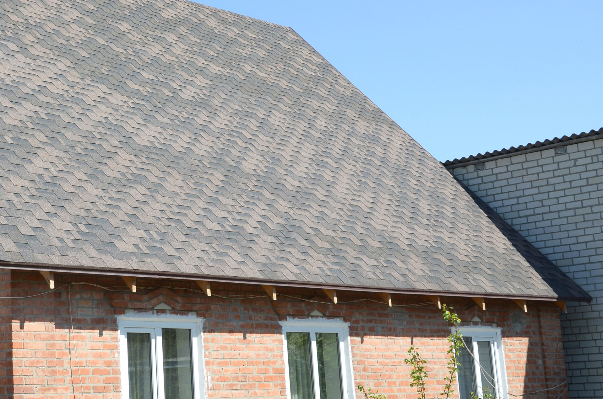 Flexible shingles of bitumen roofing surface on the brick house. Mosaic texture of flat roof tiles with bituminous coating